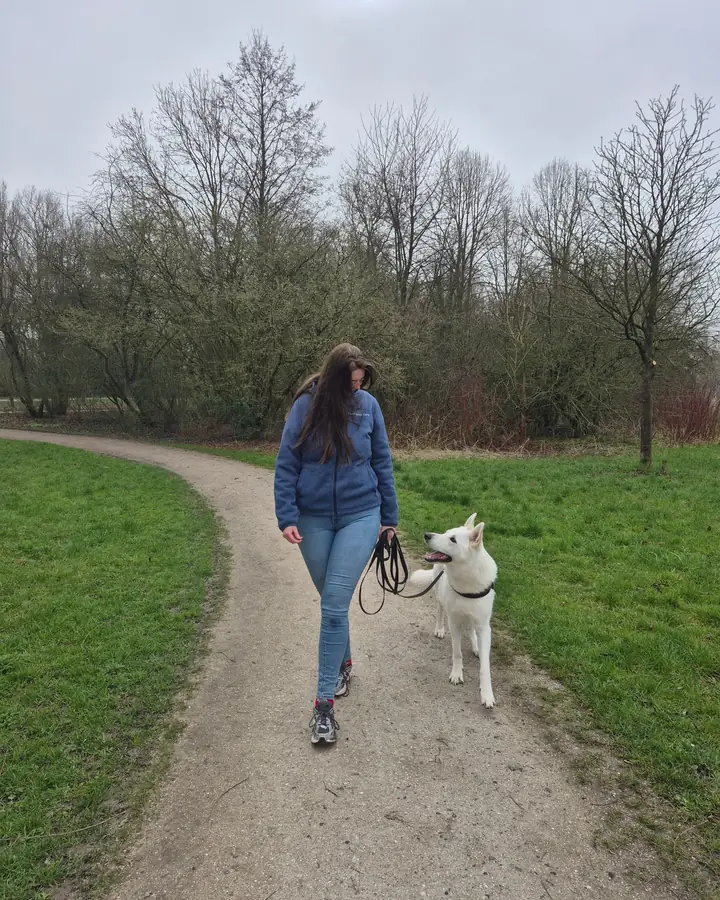 Gabey wandelt met een witte herdershond aan de lijn over een parkpad