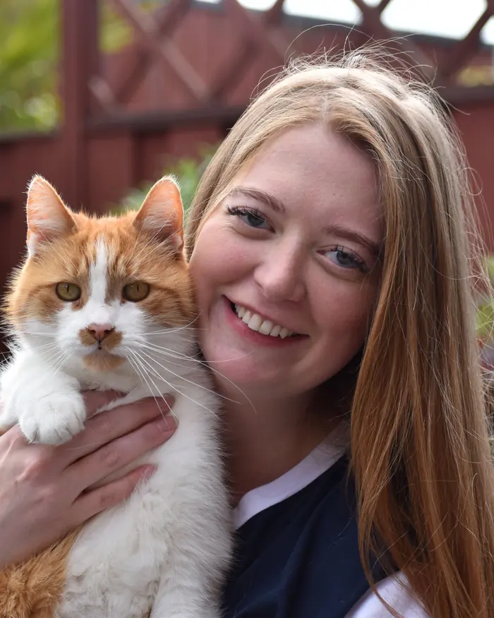 Gabey lacht in de camera met een rood-witte kat in haar armen